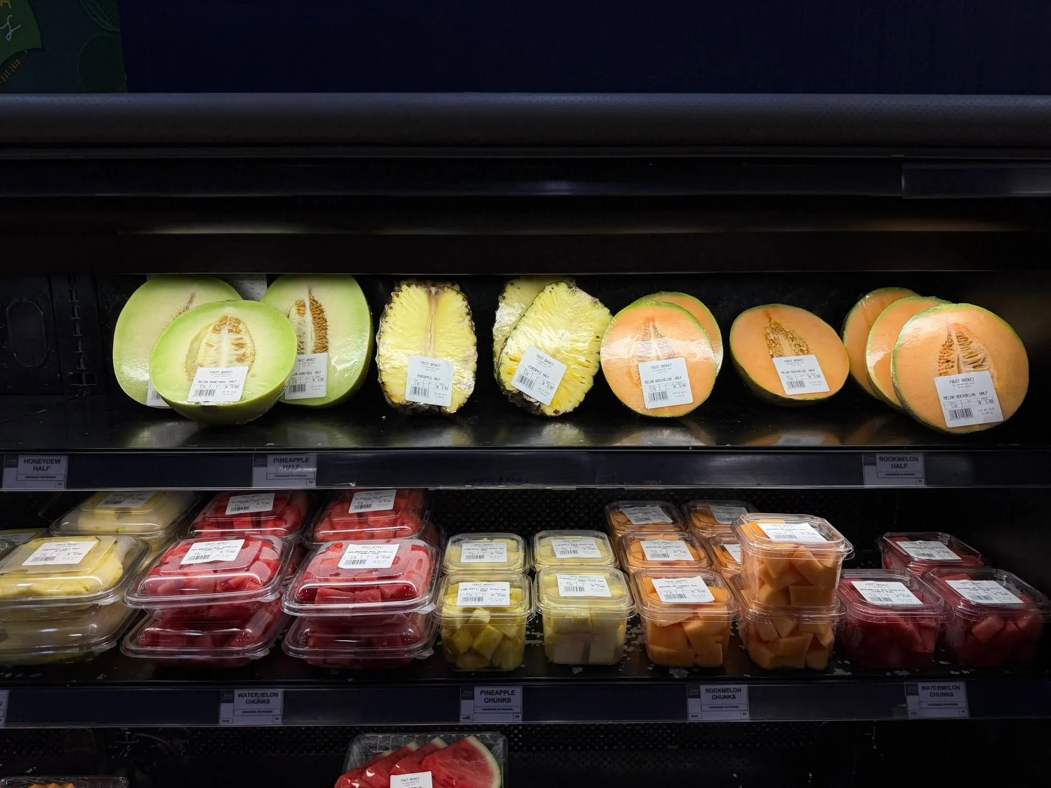 Halved cantaloupes and melons with cut fruit containers in the refrigerated case