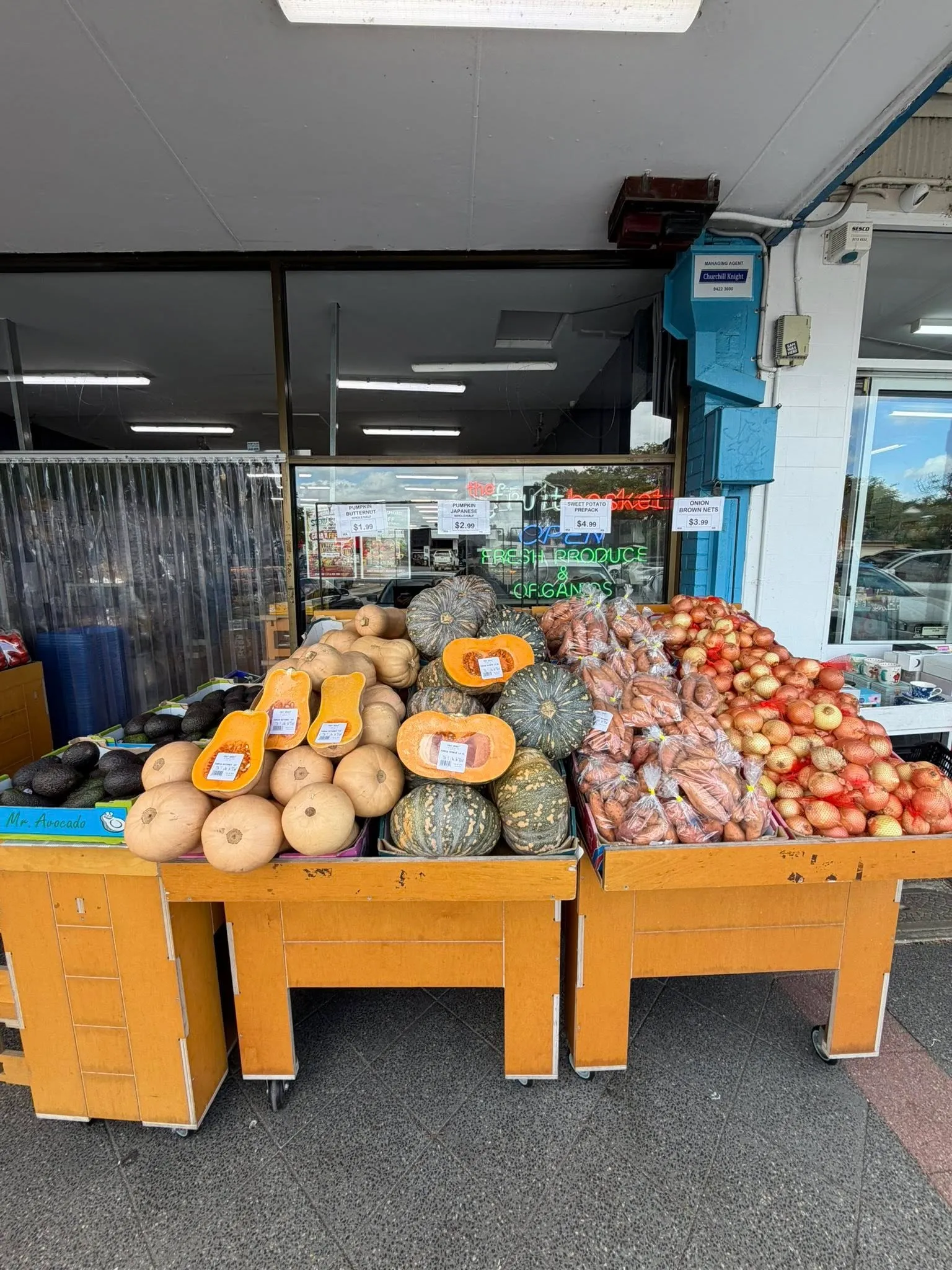 Wooden produce displays at the shop entrance with onions, pumpkins and tomatoes